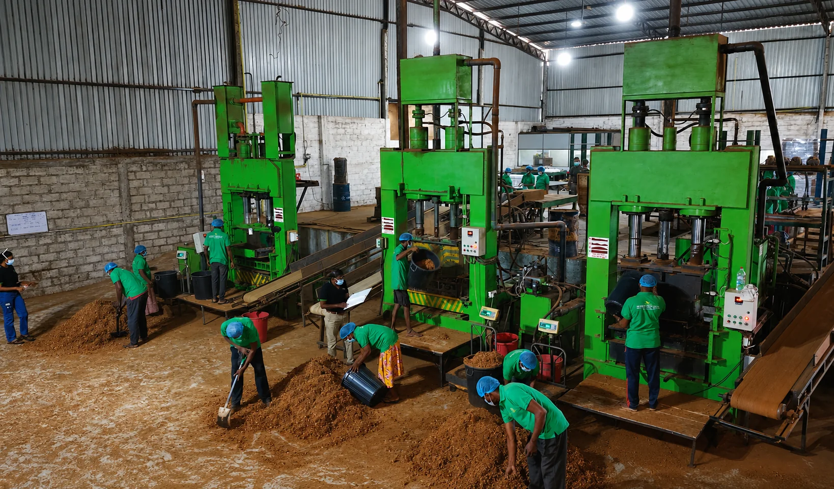 Production team operating hydraulic coco peat compression presses on the Go Green Exports factory floor in Bingiriya, Sri Lanka